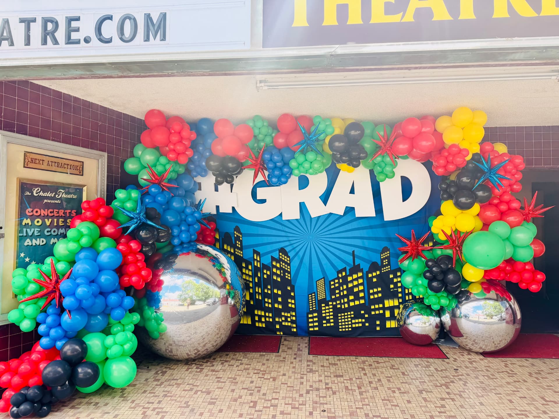 Superhero-themed graduation balloon arch framing a large #GRAD backdrop