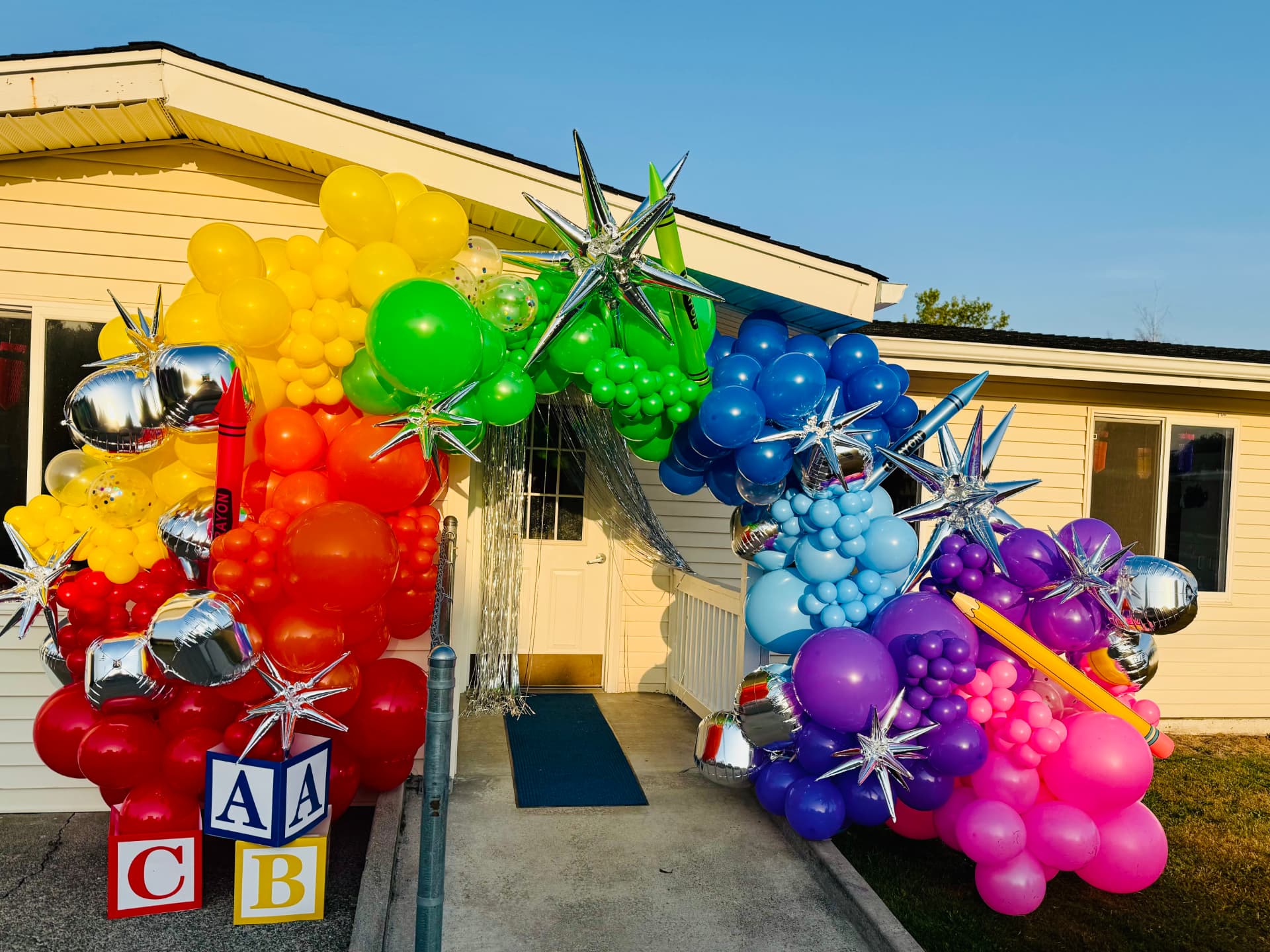 Colorful crayon balloon arch with red, yellow, green, blue and purple balloons over a school entrance